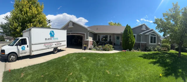 A moving truck parked in front of a gray house on a sunny day.