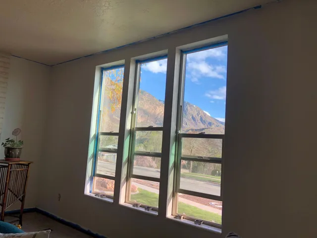 Three windows show a mountain view. Interior room has white walls and a small table.
