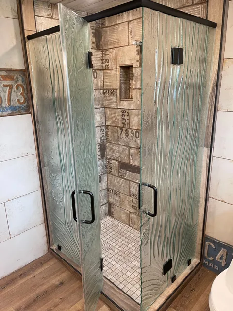 Shower with textured glass doors, dark frames, and tile walls.