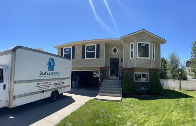 Beige two-story house with a moving truck parked in the driveway on a sunny day.